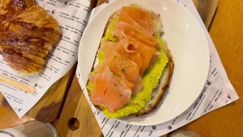 A delicious breakfast featuring smoked salmon on avocado toast and a croissant Stock Footage 276617613