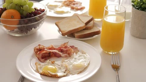 A delicious breakfast scene with eggs, bacon, toast, and juice on table. Perfect Stock Footage 276165362