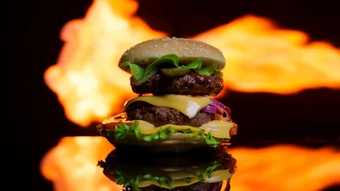Delicious burger on the black mirror surface. The fire of grill on the Stock Footage 92515220