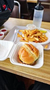 A delicious burger in a clamshell container with crinkle-cut fries on a plate Stock Photos