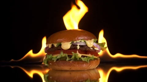 A delicious Burger on a mirrored table Fire appears in the background. Stock Footage 125655643