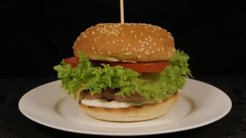 Delicious burger rotating on a white plate isolated on black background Stock Footage 314330025