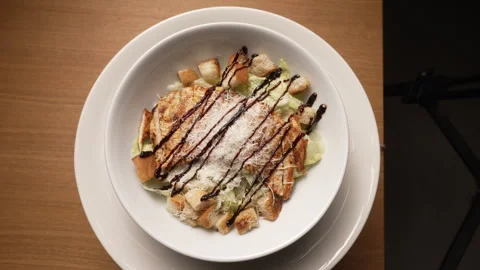 Delicious chicken caesar salad spinning in a white bowl with parmesan cheese Stock Footage 336678094