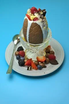 Delicious chocolate Easter egg topped with ice cream, berries, cookies, custard Stock Photos