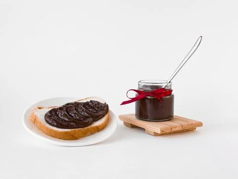 Delicious chocolate spread on bread with jar tied with red ribbon Stock Photos