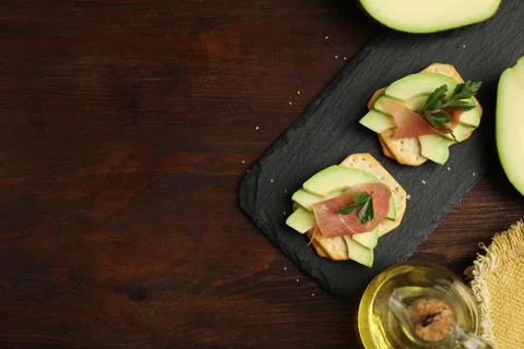 Delicious crackers with avocado, prosciutto and parsley on wooden table, flat Stock Photos