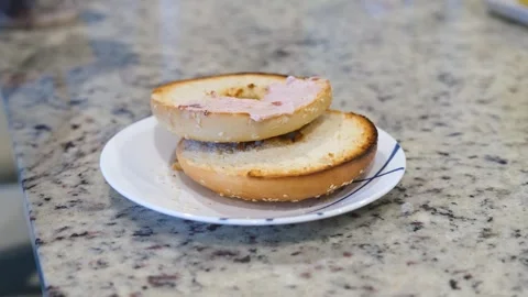 Delicious cream cheese spread on toasted bagel in cozy kitchen setting Stock Footage 302412143