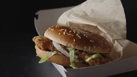 A delicious crispy chicken burger rotates on a dark background, showcasing its g Stock Footage 302984584