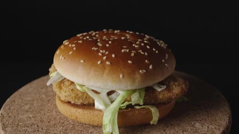 A delicious crispy chicken burger rotates on a dark background, showcasing its g Stock Footage 302984589