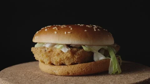 A delicious crispy chicken burger rotates on a dark background, showcasing its g Stock Footage 302984671