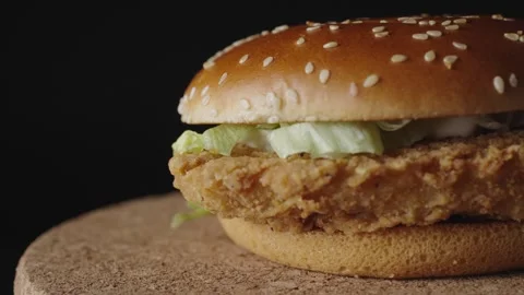 A delicious crispy chicken burger rotates on a dark background, showcasing its g Stock Footage 302984672