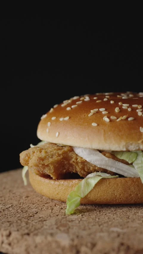 A delicious crispy chicken burger rotates on a dark background, showcasing its g Stock Footage 302986142