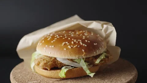 A delicious crispy chicken burger rotates on a dark background, showcasing its g Stock Footage 302986143
