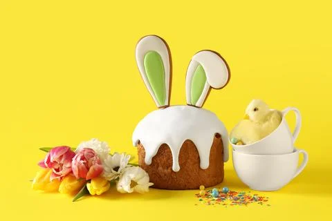 Delicious Easter cake with bunny ears, tulip flowers and cups on yellow backg Stock Photos