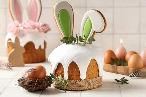 Delicious Easter cakes with bunny ears, roses, leaves and eggs on white tile  Stock Photos