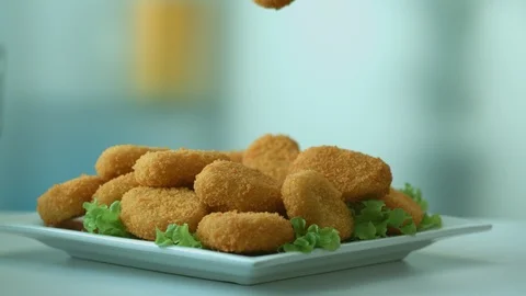Delicious fresh fried nuggets fall into a plate with a green leaf of lettuce Stock Footage 116874419