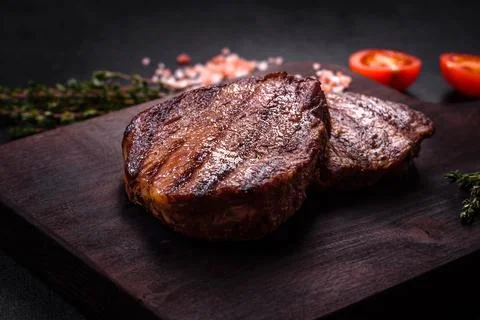 Delicious fresh juicy beef steak with spices and herbs on a dark concrete b.. Stock Photos