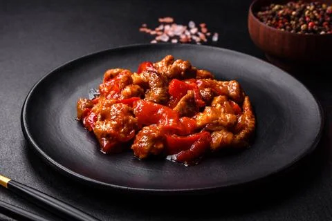 ..Delicious juicy meat with hot peppers and sauce on a black ceramic plate on Stock Photos
