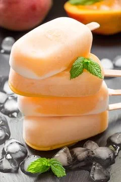Delicious mango ice cream popsicles stacked on a dark surface surrounded by ice Stock Photos