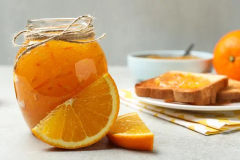 Delicious orange marmalade in glass jar on light grey table. Space for text Stock Photos