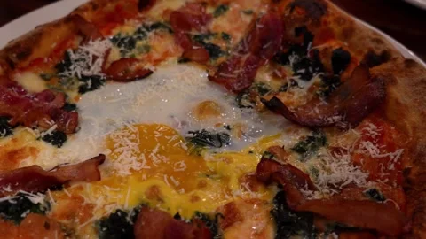Delicious pizza with egg, spinach, bacon, and cheese on a white plate Video stock 306738955