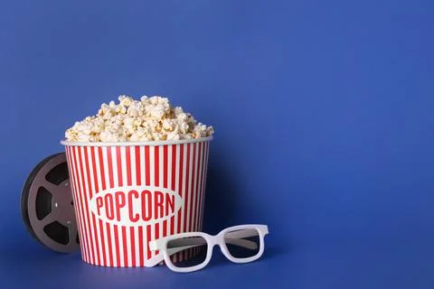 Delicious popcorn, 3D glasses and movie reel on blue background. Space for te Stock Photos