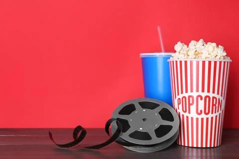 Delicious popcorn, drink and movie reel on wooden table. Space for text Stock Photos