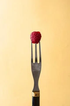 Delicious raspberry on a fork an dark yellow background and copy space on the Stock Photos