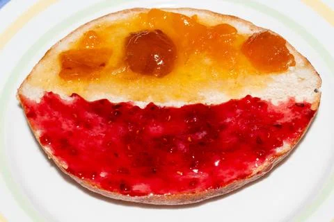A delicious slice of bread with bright red raspberry jam and golden apricot Stock Photos