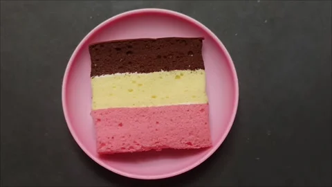 A delicious slice of Neapolitan cake on a pink plate Video stock 323579662
