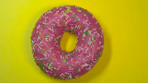 Delicious sweet donut quickly rotating on a yellow background.. Top view. Stock Footage 87991806