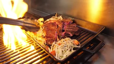 A delicious, thick-cut T-bone steak is cooked and served on a hot griddle with f 스톡 동영상 332815240