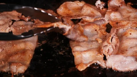 Delicious thin sliced bacon frying on the iron in slow motion Stockbeeldmateriaal 95282617