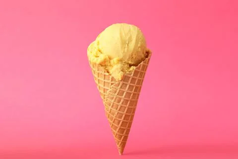 Delicious yellow ice cream in waffle cone on pink background Stock Photos