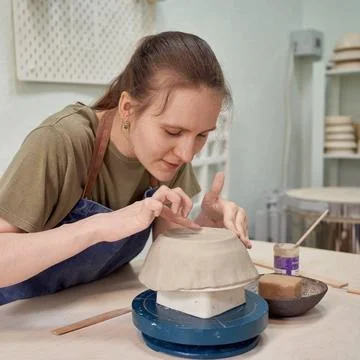 Delight female apprentice working on pottery bowl in workshop Concentrated... Stock Photos
