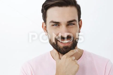 Delighted charming and charismatic bearded male with dark hair rubbing chin with Stock Photos