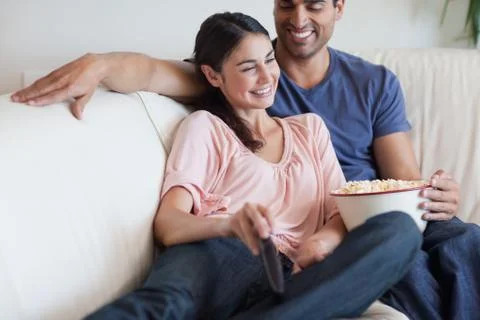 Delighted couple watching TV while eating popcorn Stock Photos