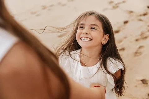 Delighted cute child smiling while having fun with anonymous mom on beach Stock Photos