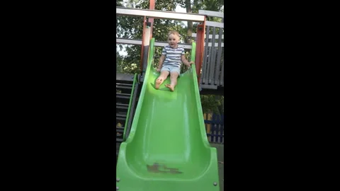 A delighted little boy slides down a plastic slide at a playground. Stock Footage 282517671