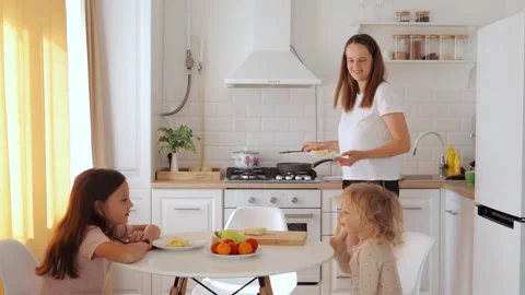 Delighted mom serving healthy omelets to her kids at the kitchen table while the Видео 291280137