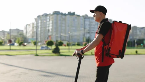 Deliverman courier with isothermal backpack case pizza box rides his electric Stock Footage 194597992