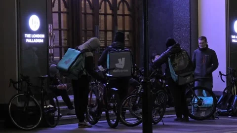Deliveroo food delivery drivers sitting on steps outside a theatre in London Stock Footage 143354853