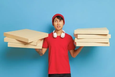 Delivery Asian guy dressed in red hat and red t-shirt holding cardboard pizza Stock-Fotos