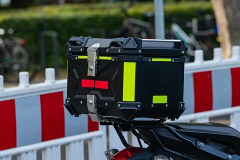 Delivery box placed on the motorcycle parked near barrier Stock Photos