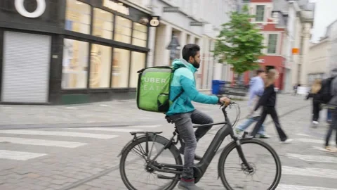 Delivery boy with Deliveroo jacket and Uber Eats thermal bag cycling on Stock Footage 196849267