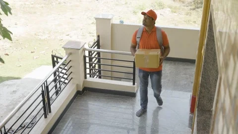 Delivery boy placing parcel in front of door after showing parcel to cctv or Stock Footage 169149854