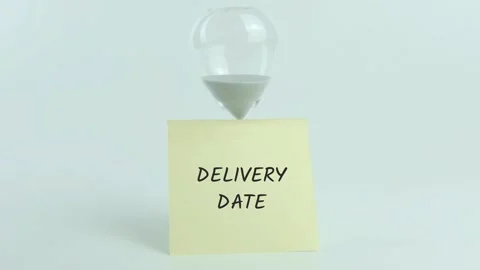 Delivery date written on yellow sticky note placed on hourglass on white Stock Footage 313474199
