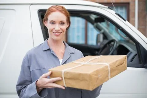 Delivery driver smiling at camera by her van holding parcel Stock Photos