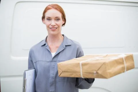 Delivery driver smiling at camera by her van holding parcel 库存照片
