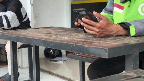 Delivery driver taking a break, engaged with smartphone at a rustic outdoor.. Vidéo 325234534